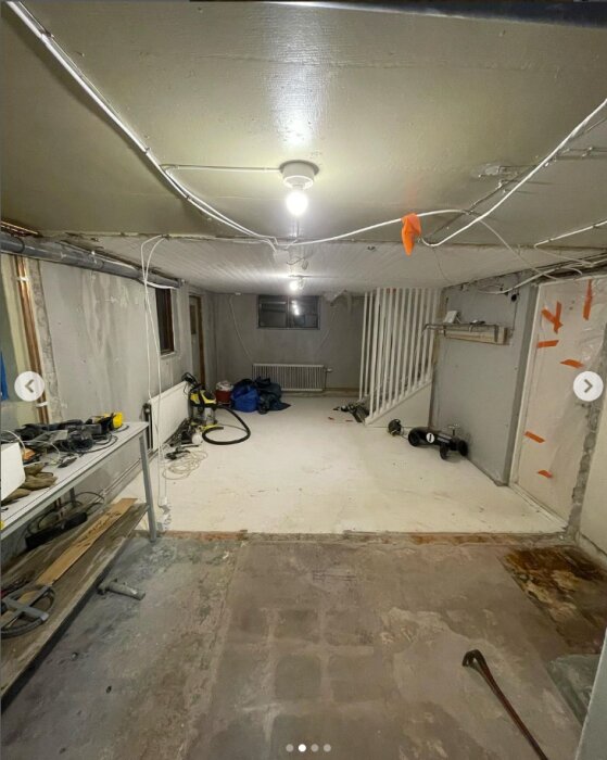 Källarutrymme under renovering med synliga verktyg, kablar i taket och borttagen tegelvägg, visar status för byggprojekt.