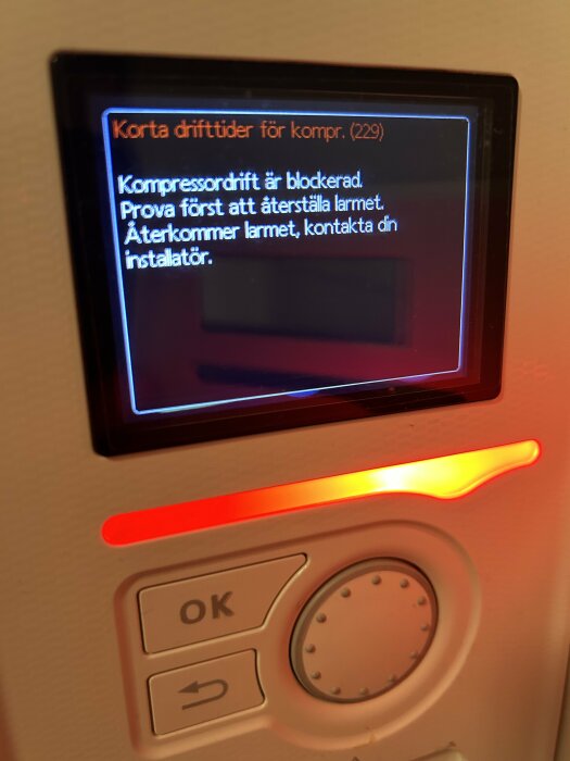 Felmeddelande på en kontrollpanel visar "Kompressordrift är blockerad" med en röd lysande indikation och knappar för OK och bakåt.