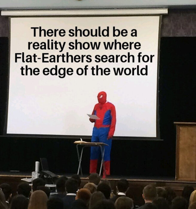 Person i Spiderman-dräkt talar inför publik med texten: "There should be a reality show where Flat-Earthers search for the edge of the world" på projektorduk.