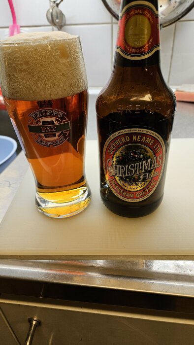 En flaska och ett glas Shepherd Neame Christmas Ale, en stark engelskt julöl, på en köksbänk med skummande öl i glaset.