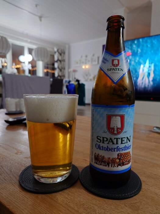 En ölflaska och ett glas med Spaten Oktoberfestbier på ett bord i ett vardagsrum.