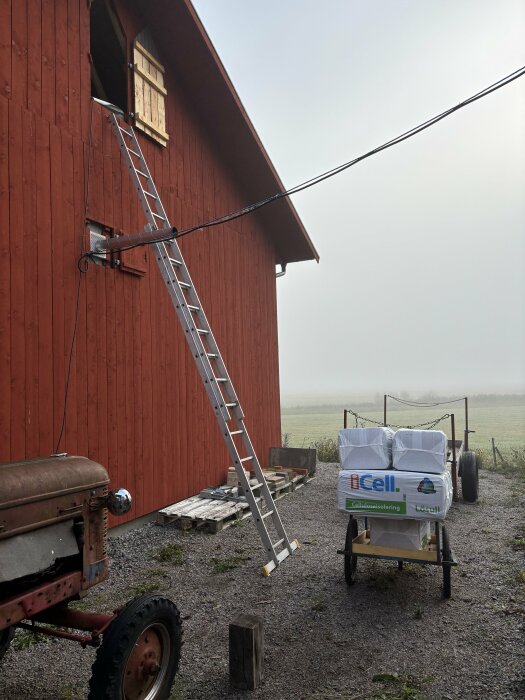 Stege lutad mot en röd träbyggnad vid en öppning, bredvid en kärra med isoleringsmaterial iCell.