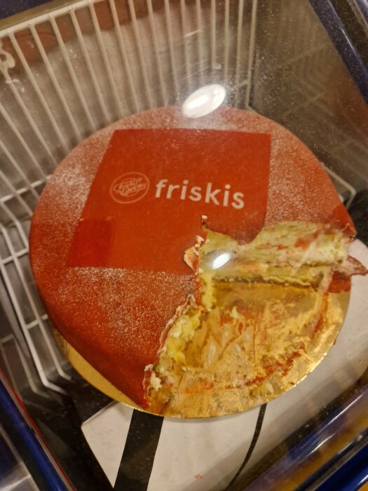 Tårta i kyldisk med röd marsipan och texten "friskis" på toppen, en bit saknas.