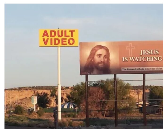 Två skyltar, en med texten "ADULT VIDEO" och en billboard med en bild av Jesus och texten "JESUS IS WATCHING" i landskapsmiljö.