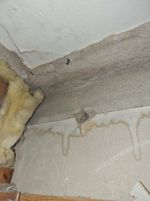 Gråaktig isolering synlig i ett gammalt tak från ett hus byggt runt 1900, med texturer och fuktskador på väggen.