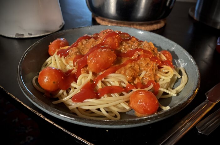 Spagetti med köttfärssås toppad med körsbärstomater och ketchup på en tallrik.