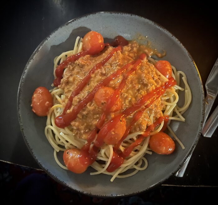 Tallrik med spaghetti och köttfärssås, dekorerad med körsbärstomater och ketchup.