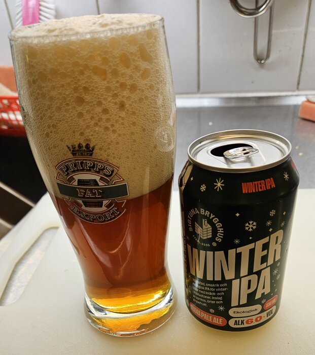 Ölglas med skummande Winter IPA från Sigtuna Brygghus bredvid en öppnad burk, båda placerade på en köksyta.