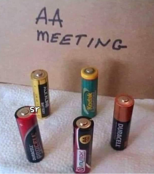 Fem AA-batterier står uppradade med texten "AA Meeting" skrivet i bakgrunden på en kartong.