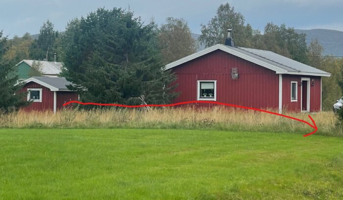 Röd stuga i gräsmark med en röd pil som visar flyttriktning. Skog och fjäll i bakgrunden, kranbil ska parkera vid grönt område. Skymd fjällsjöutsikt.