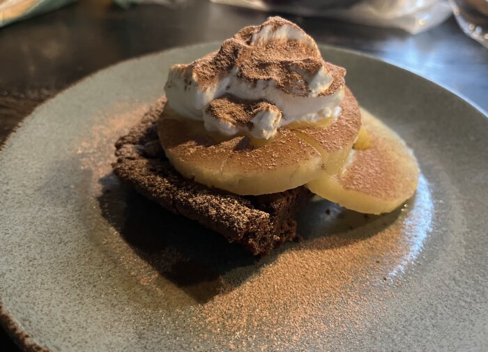 Kladdkaka med ananas, vispad grädde och pudrad kakao serveras på en tallrik.