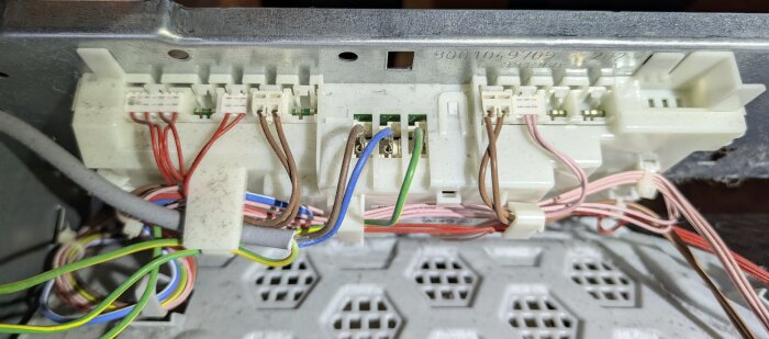 Närbild på elektronikkort med flera anslutna kablar i en trasig Bosch torktumlare, delvis demonterad för reparation av kretskort och relä.