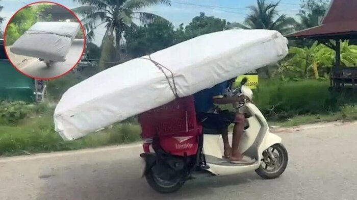 Man transporterar en sex fot lång madrass på en motorcykel.