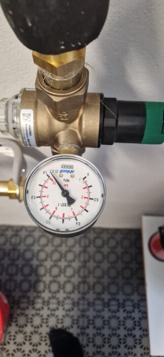 Manometer visar vattentryck över 10 bar vid inkommande regulator, med synlig del av rörledning och koppling mot ljus bakgrund.