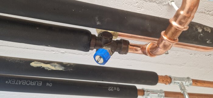 Ventil med blått handtag på kopparrör, del av vattenanslutning till bergvärmepump.