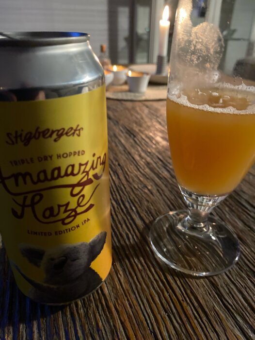 Burk och glas med Stigbergets Amaaazing Haze IPA på ett bord med levande ljus.