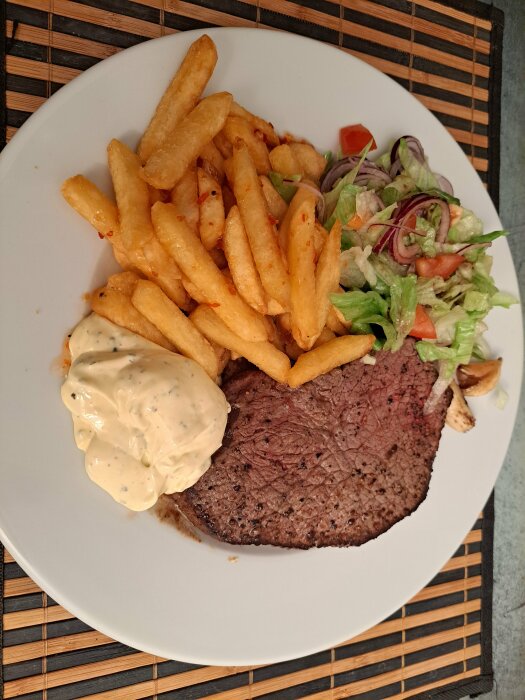 Tallrik med biff, pommes frites, sås och sallad.