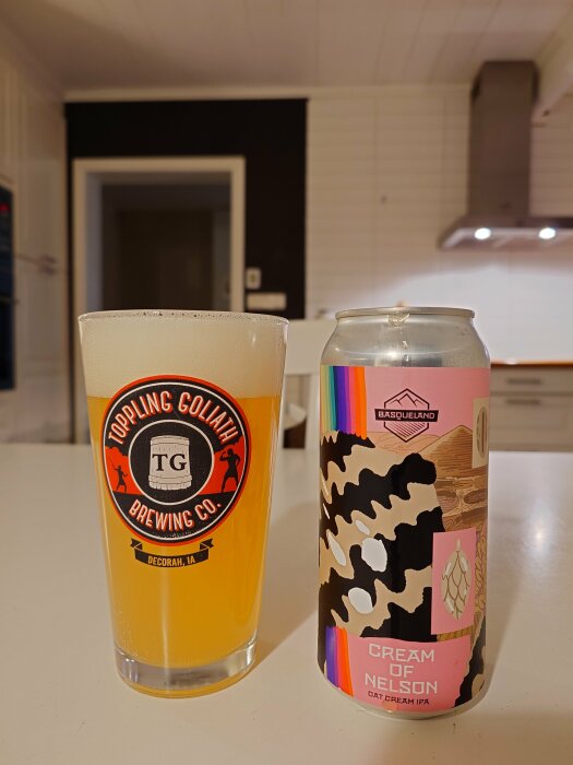 Ett glas öl från Toppling Goliath Brewing Co. och en burk Cream of Nelson Oat Cream IPA från Basqueland på ett köksbord.