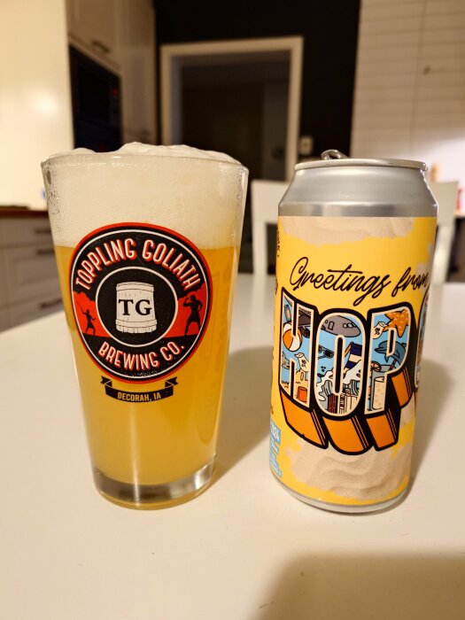 Glas med öl från Toppling Goliath Brewing Co. bredvid en burk med etiketten "Greetings from Hop".