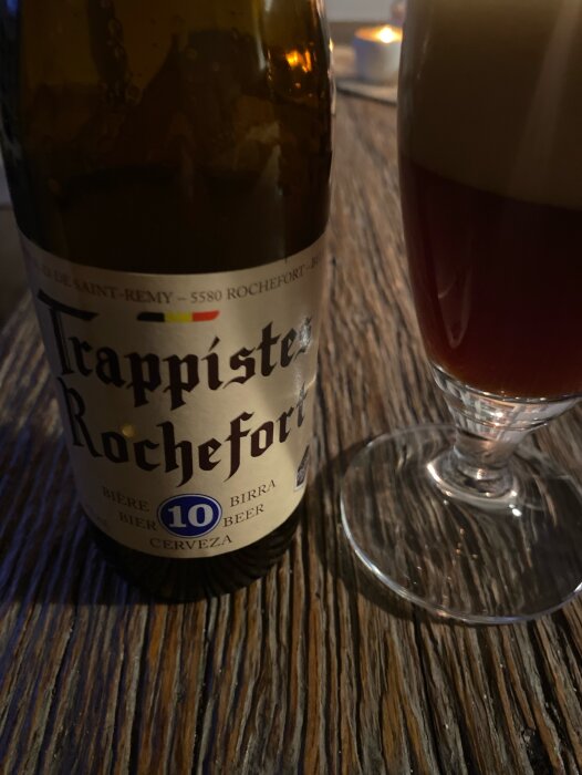 Flaska och glas av Trappistes Rochefort öl på ett träbord med skummande dryck.