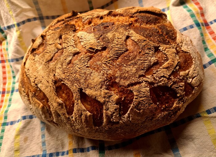 Rustikt bröd med krispig skorpa på färgglad kökshandduk.