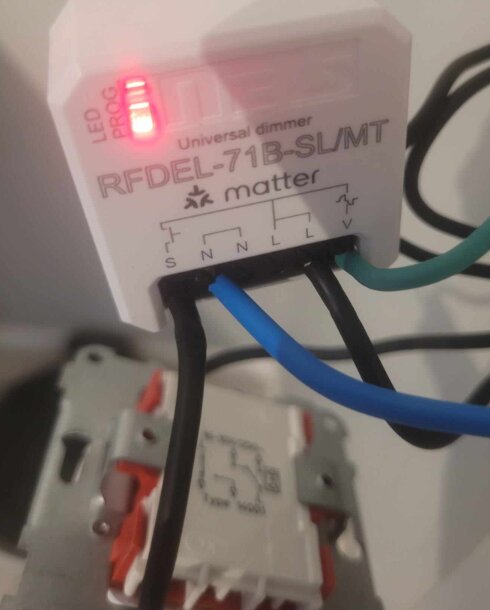 Närbild på en universell dimmer RFDEL-71B-SL/MT med elledningar anslutna, visande lysdioder och kopplingsdiagram i bakgrunden.