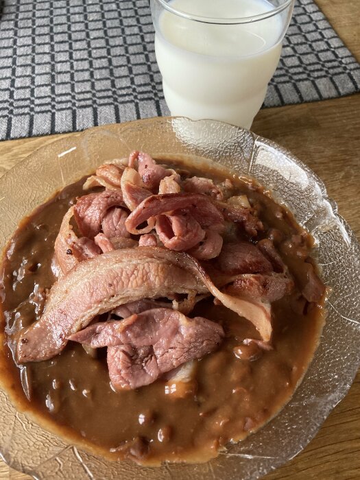 Tallrik med bruna bönor och stekt fläsk samt ett glas mjölk på ett bord.