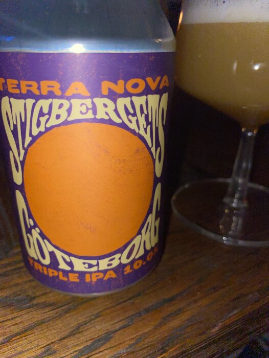 En burk Stigbergets Terra Nova Triple IPA med en del av ett glas öl i bakgrunden.
