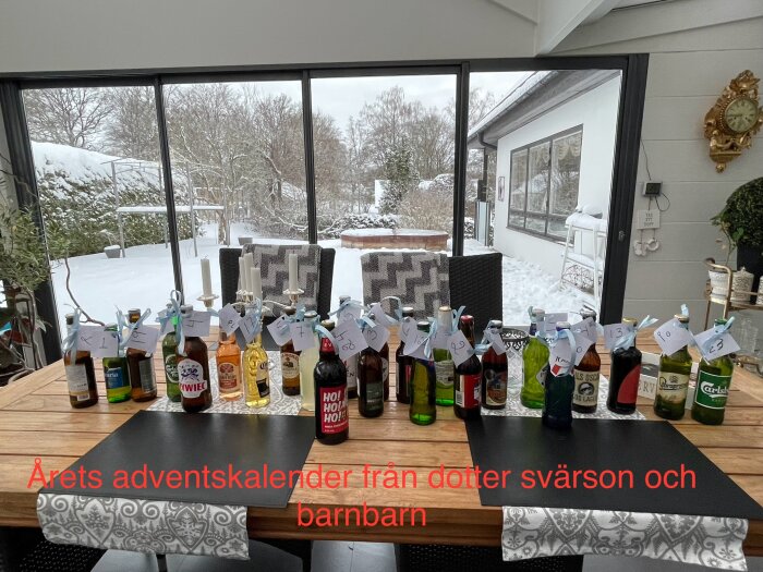 Adventskalender med flaskor på ett bord i vinterträdgård, skapad av dotter, svärson och barnbarn. Flaskorna har numrerade lappar.