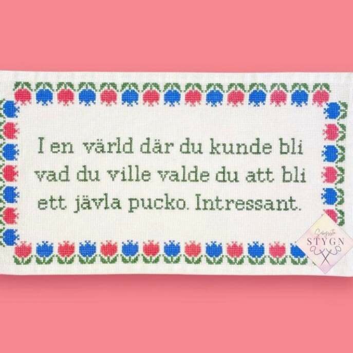 Broderad tavla med texten: "I en värld där du kunde bli vad du ville valde du att bli ett jävla pucko. Intressant." Omgiven av blommönster.