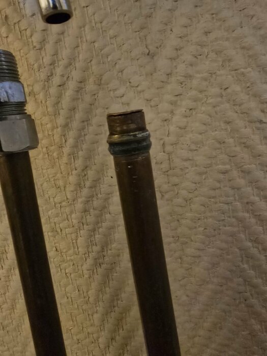 Två rörändar i metall, varav den ena ser kapad ut. De ligger mot en mönstrad yta som kan vara en vägg eller golv.