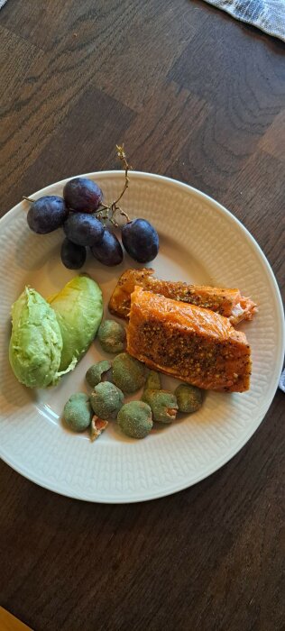 Tallrik med avokado, vindruvor, kryddad lax och gröna bär på ett träbord.