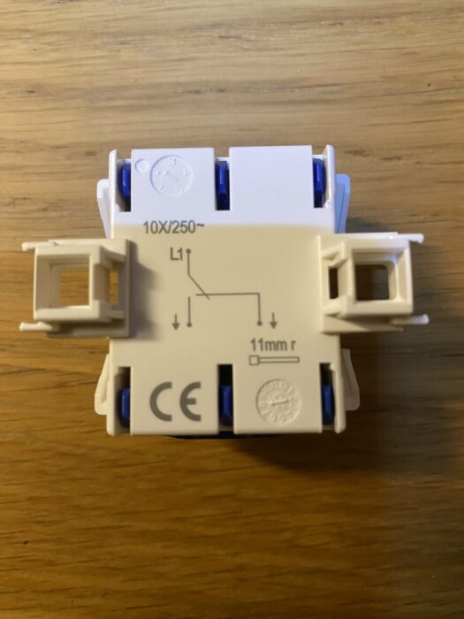En bild på en vit 1-polig strömbrytare med märkningar och kopplingsschema, liggande på ett träbord.