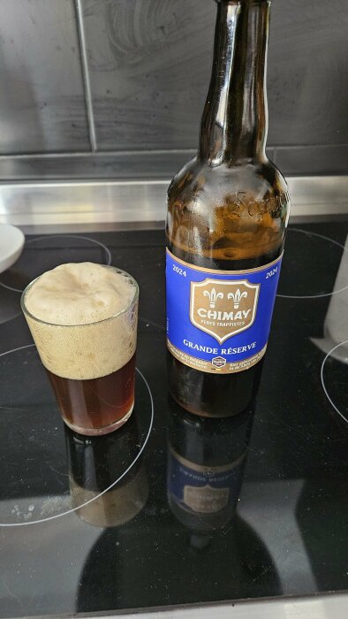 Flaska och glas fyllda med Chimay Grande Réserve-öl på en spishäll.