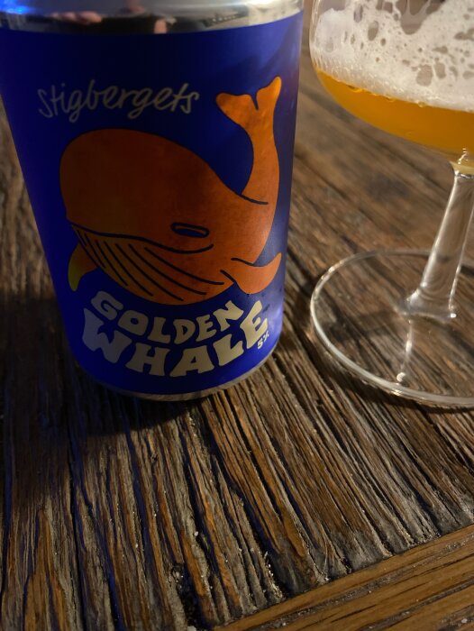 En burk Stigbergets Golden Whale öl och ett glas på ett träbord.