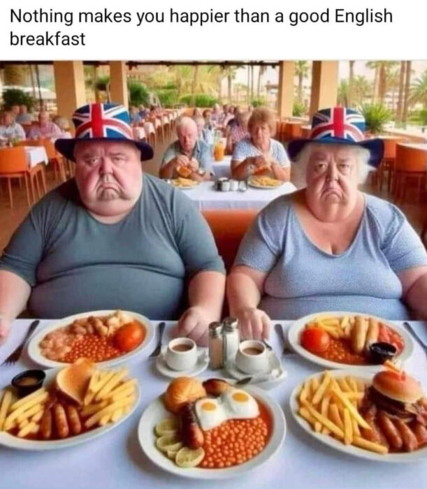 Två personer i Union Jack-hattar sitter vid ett bord fullt av engelsk frukostmat, inklusive bacon, ägg och bönor, ser missnöjda ut.