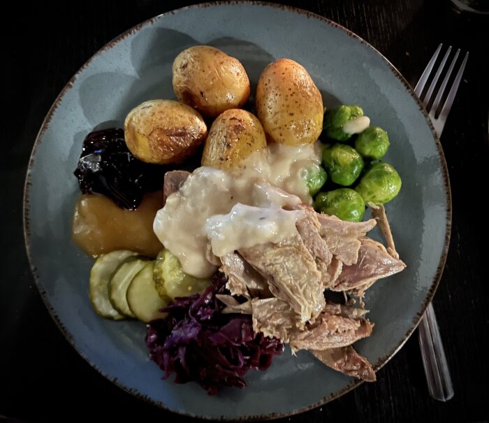 Tallrik med ugnsstekt potatis, brysselkål, rödkål, inlagd gurka, äppelmos, sås och gåskött.