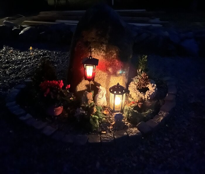 Upplyst sten med två lyktor i en trädgårdsinstallation, omgiven av blommor och dekorativa element på natten.