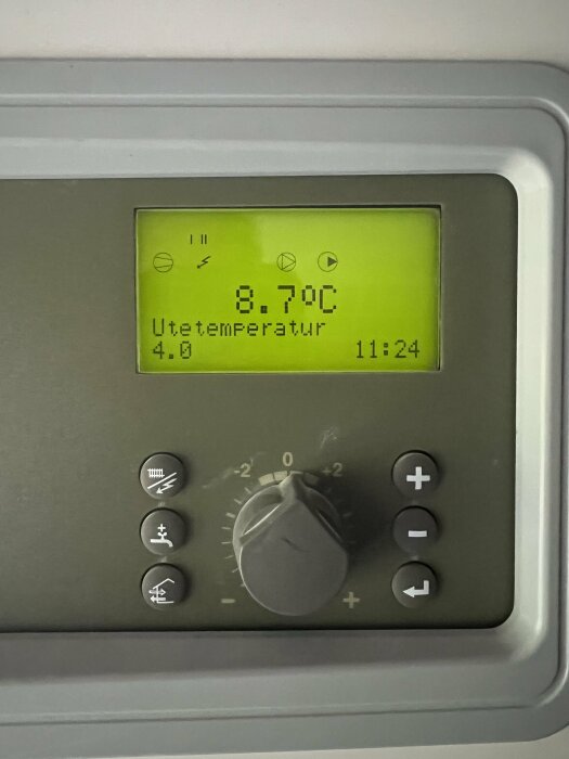 NIBE-värmepumpdisplay som visar utetemperatur 8.7°C och tid 11:24. Kontrollpanel med knappar och vred syns.