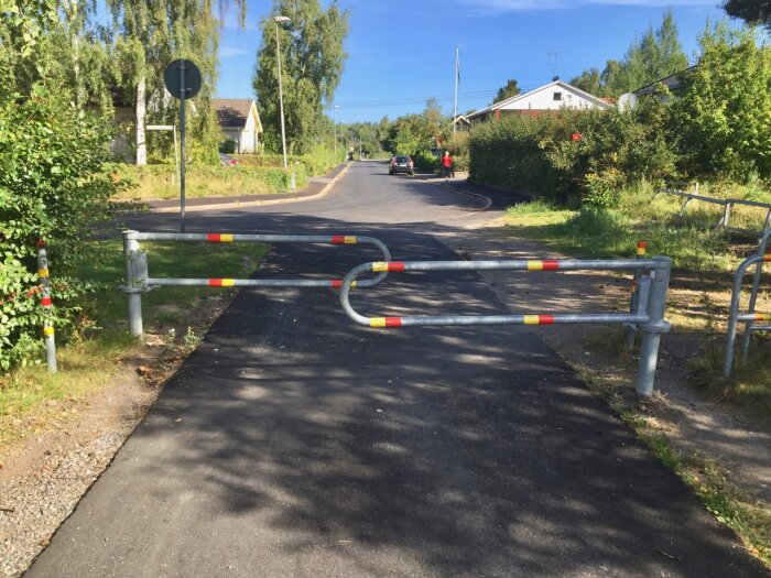 Cykel- och gångvägsväg med metallbommar målade med röda och gula markeringar som svänger undan för fordon.