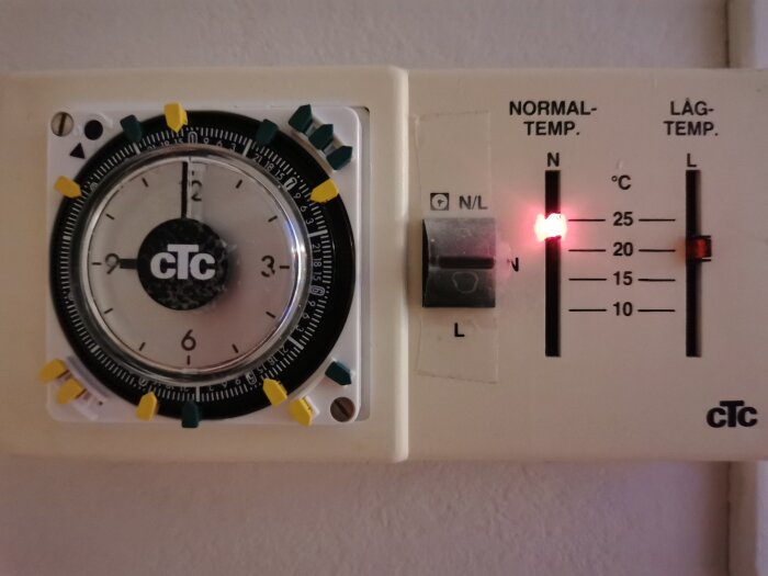 Analog timer och termostat för en gammal CTC-luftvärmepump, med rattinställningar och temperaturreglage.