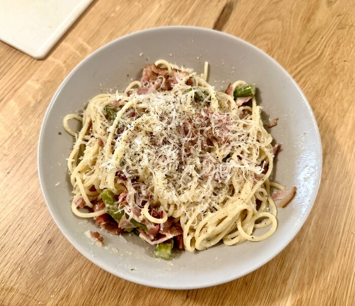 Pasta med parmesansås, sparris och vedrökt sidfläsk på en vit tallrik.