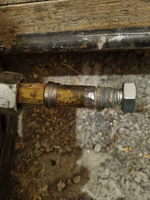 En gammal röranslutning med rost och gängor, del av ett element. En träyta och betonggolv ses i bakgrunden.