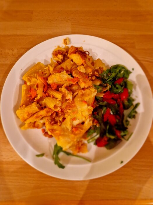 Pasta-bacon gratäng med nyriven parmesan och liten sallad på vit tallrik.