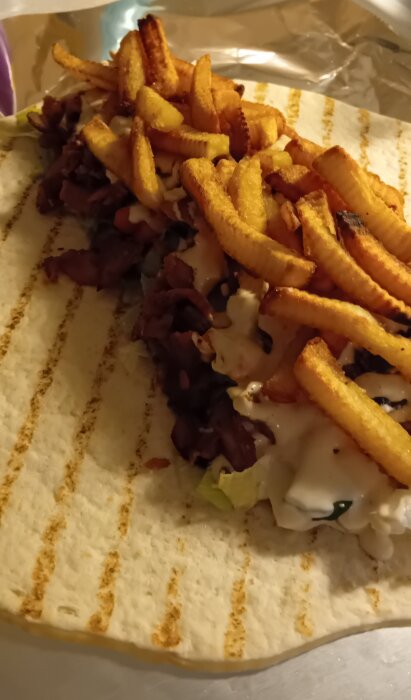 Kebabrulle fylld med kebabkött, pommes frites och sås på ett mjukt bröd, redo att rullas ihop.