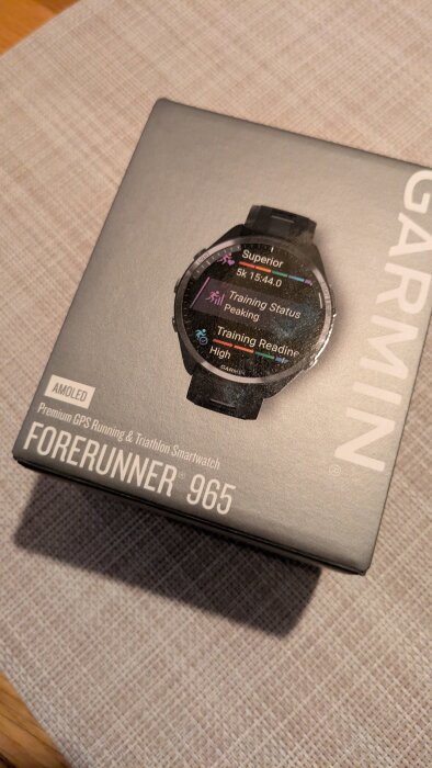 Förpackning av Garmin Forerunner 965 smartklocka med fokus på träningsstatus och prestanda på displayen.