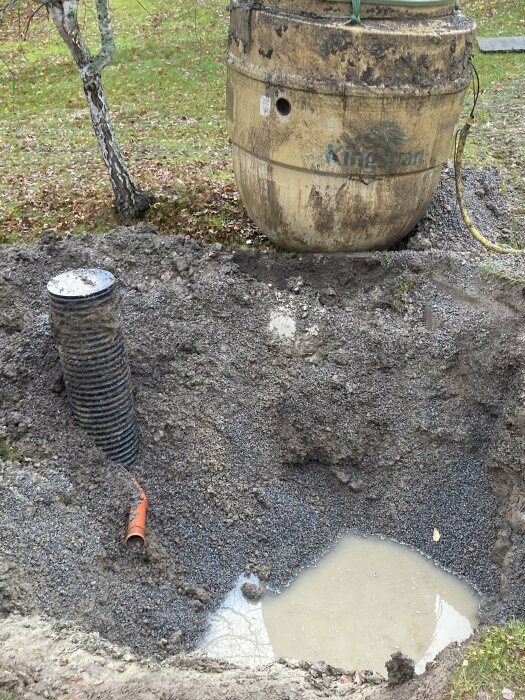 Minireningsverk som lyfts ur sin plats, synligt i hålet där det installerats, med rör och vattenpöl runt omkring, omgiven av gräs och träd.