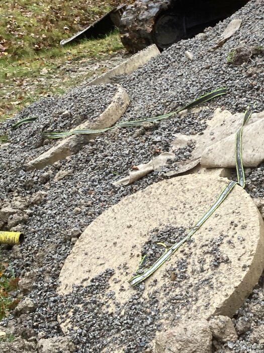 Betongfundament täckta med grus och gröna kablar på en byggarbetsplats.