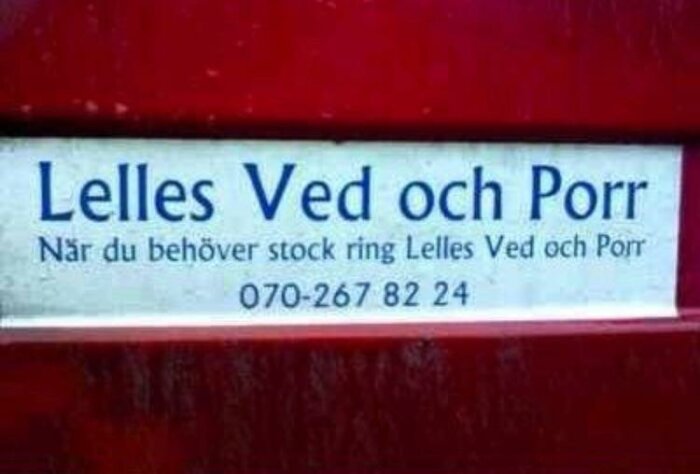 Skylt med texten "Lelles Ved och Porr - När du behöver stock ring Lelles Ved och Porr", inklusive ett telefonnummer, monterad på en röd yta.