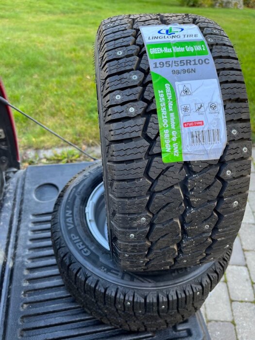 Två dubbdäck med märkningar "Linglong Tire" och "Green-Max Winter Grip Van 2". Däcken ligger på ett flak, med grönt gräs i bakgrunden.